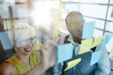 Two creative millenial small business owners working on social media strategy brainstorming using adhesive notes in windows-1